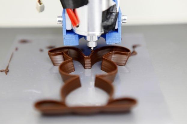 El químico y cocinero Gaëtan Richard, uno de los fundadores de Miam Factory. A la derecha, una de las impresoras en 3D, trabajando con el chocolate. ::