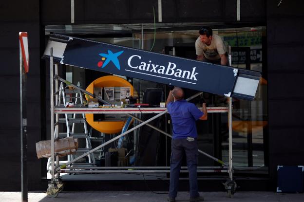 Oficina del Banc Sabadell en Alicante. :: r. c.Operarios con un cartel de CaixaBank en Barcelona. :: reuters/