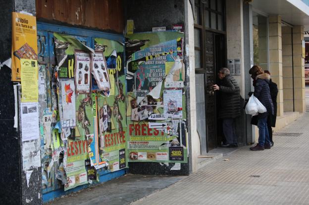 Unas personas acceden a su casa en la calle de la Vega junto a un local cerrado lleno de cartelería./ D.M.A.